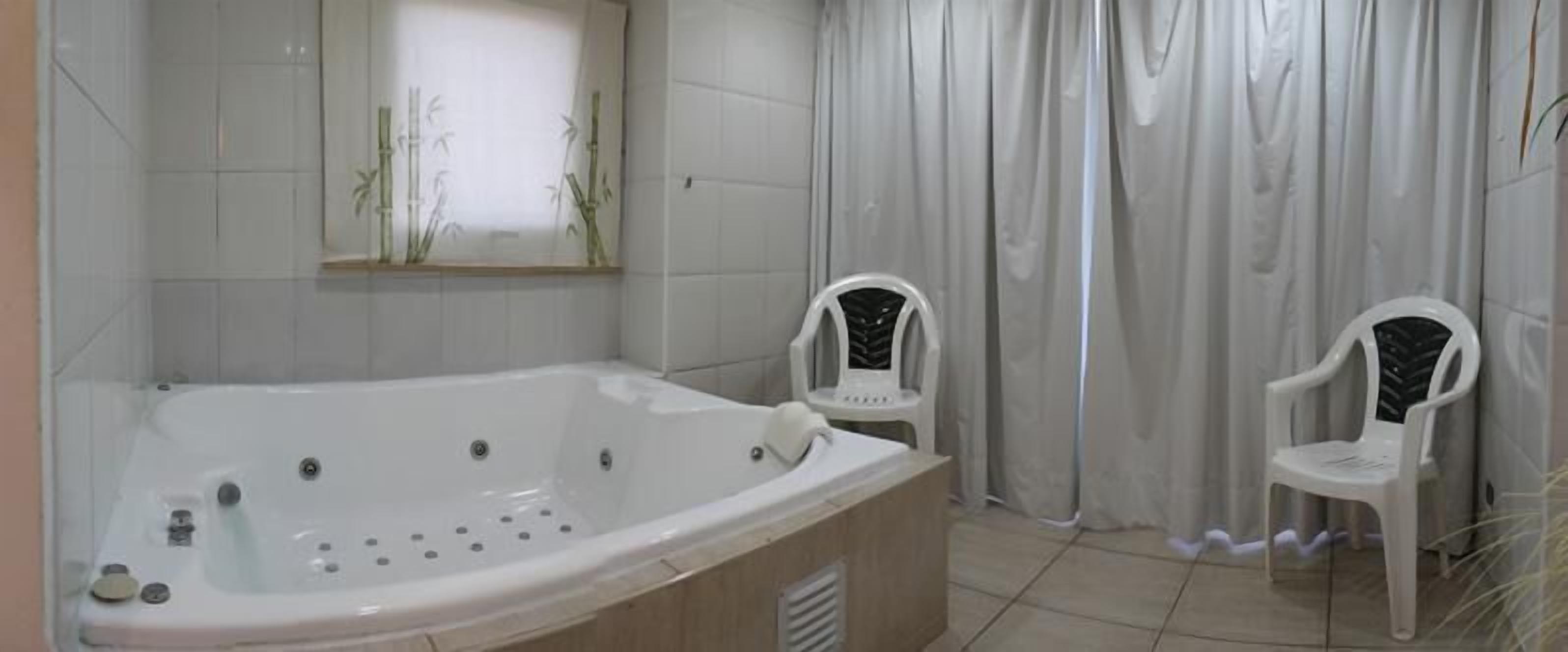 Un baño con una bañera grande, dos sillas de plástico blanco y una ventana decorada con bambú.