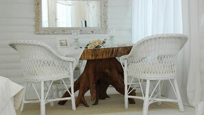 Une pièce comprenant une table en bois et deux chaises en osier blanches, un miroir avec un cadre orné et un vase rempli de fleurs.