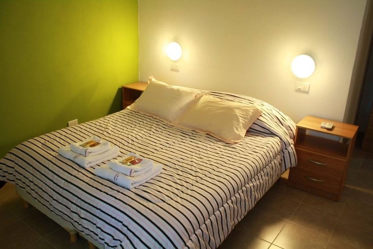 A neatly made bed with striped bedding and pillows, a bedside table with a lamp, and a wall socket.