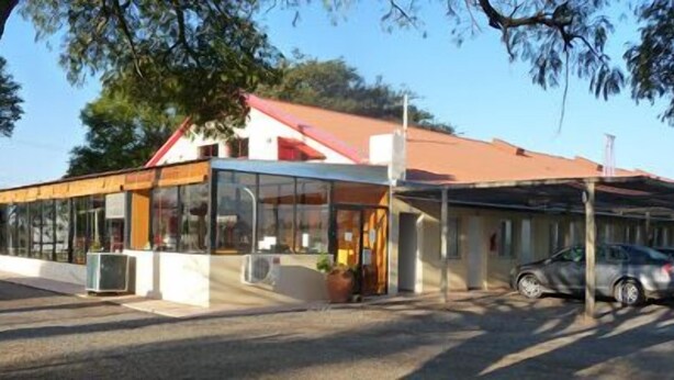 A building with a glass facade and a red roof, featuring a carport with parked cars. - Hotel Sanguinetti (Victoria)