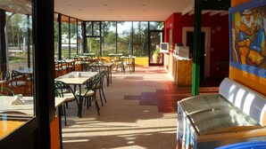 An indoor dining area with tables and chairs, a counter with a television, and large windows offering a view of the outdoors. - Hotel Sanguinetti (Victoria)