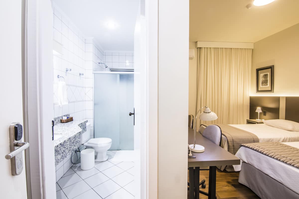 Una habitación de hotel con baño, una cama, un escritorio y una mesita de noche.