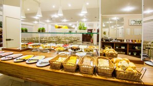 A buffet with various food items and baskets of bread. - JR Hotel (Marilia)