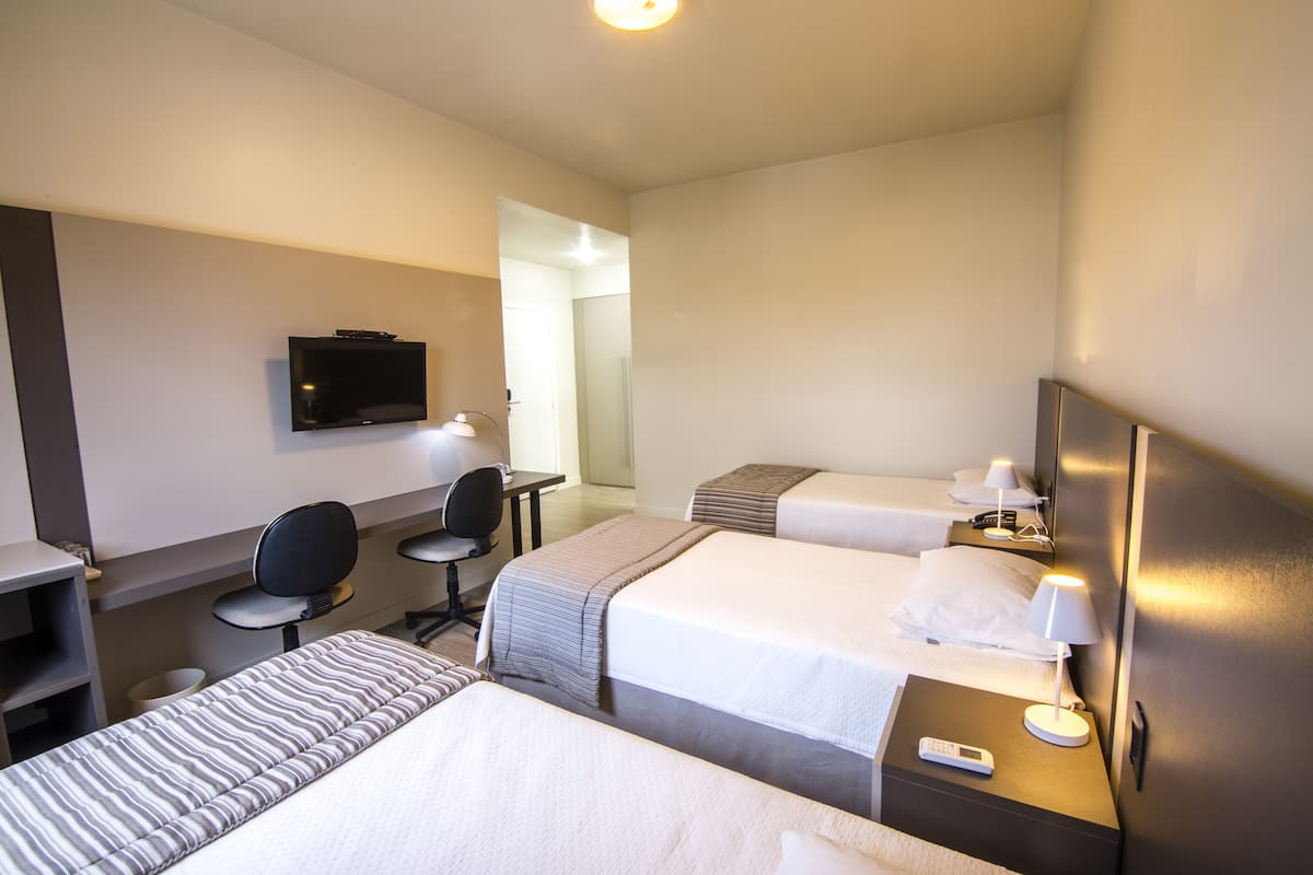 Habitación de hotel con dos camas, un escritorio con silla, televisor y lámpara.