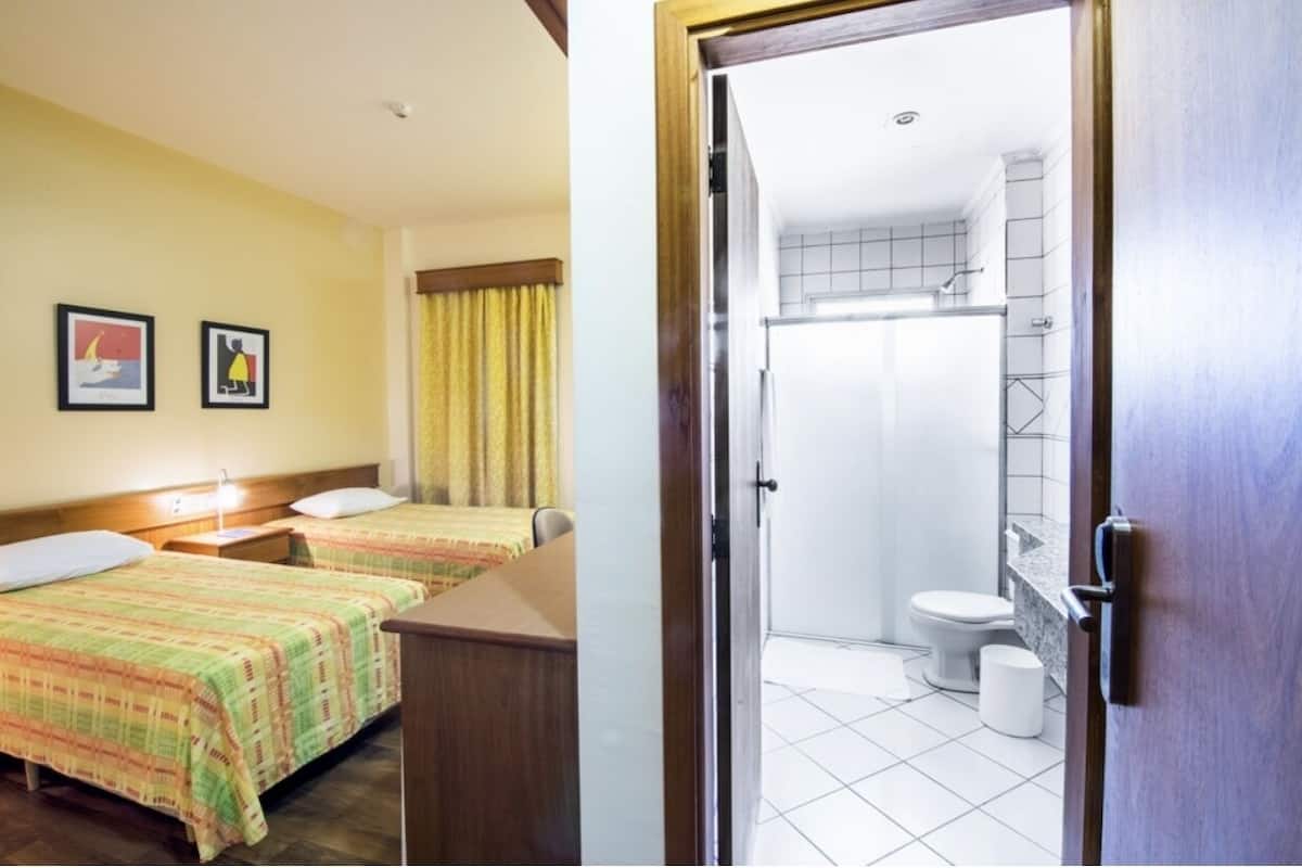 Habitación de hotel con dos camas, un escritorio de madera y un baño con ducha e inodoro.