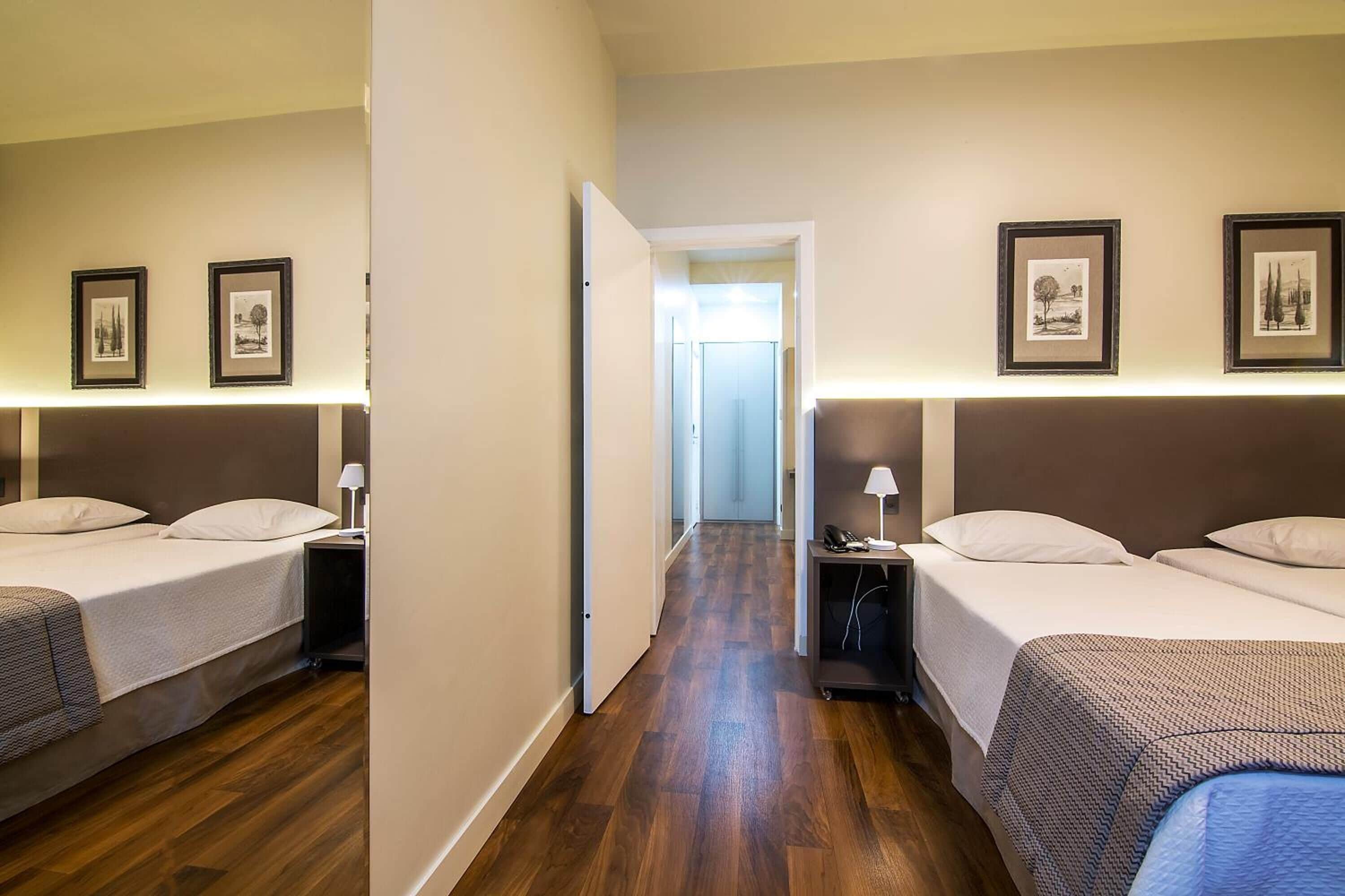 Quarto de hotel com duas camas, piso de madeira e quadros nas paredes.