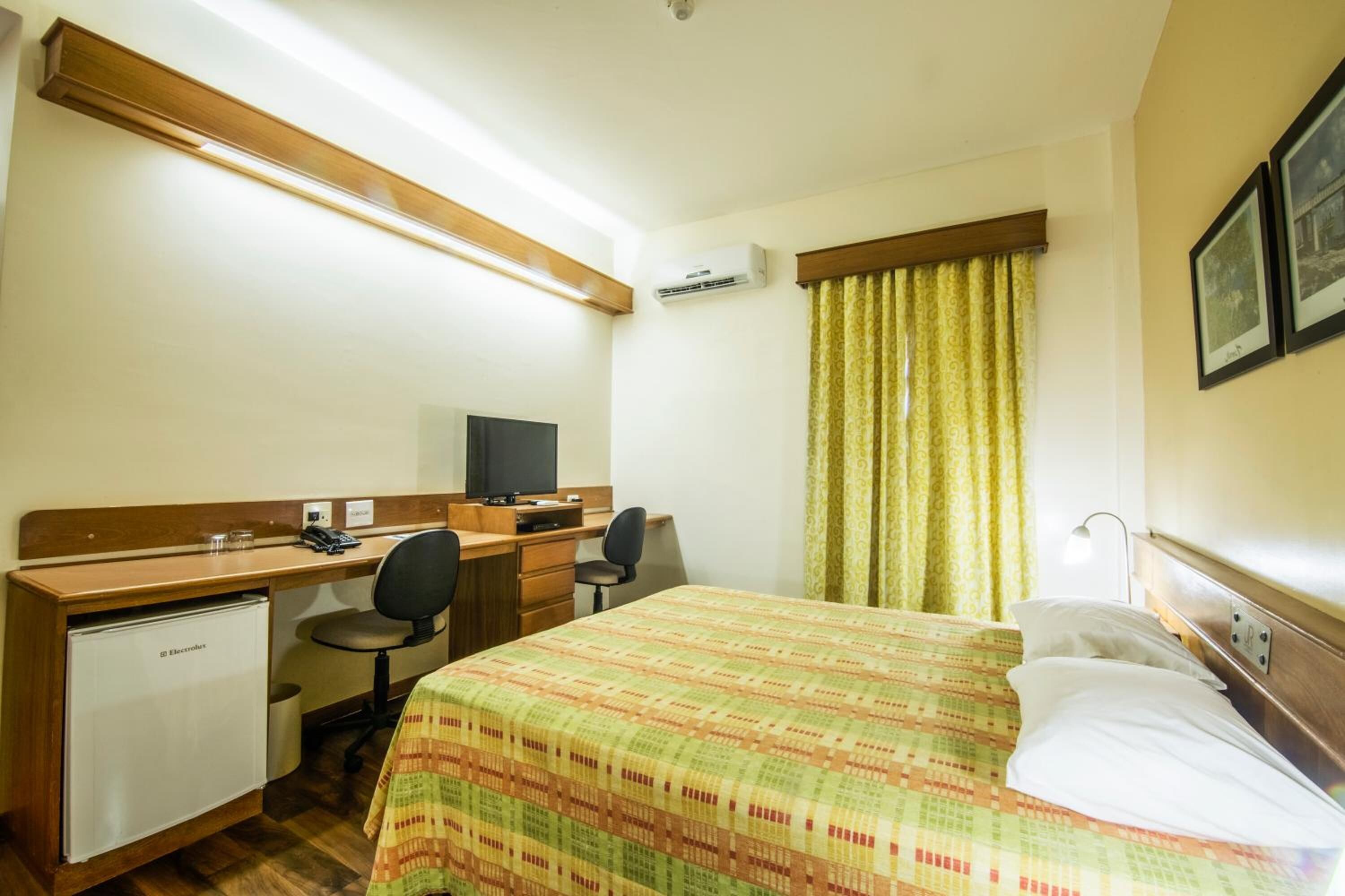 A hotel room with a bed, desk, chair, and a small refrigerator.
