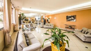 A spacious living area with a sofa, armchairs, a coffee table, and a yellow plant. - JR Hotel (Marilia)