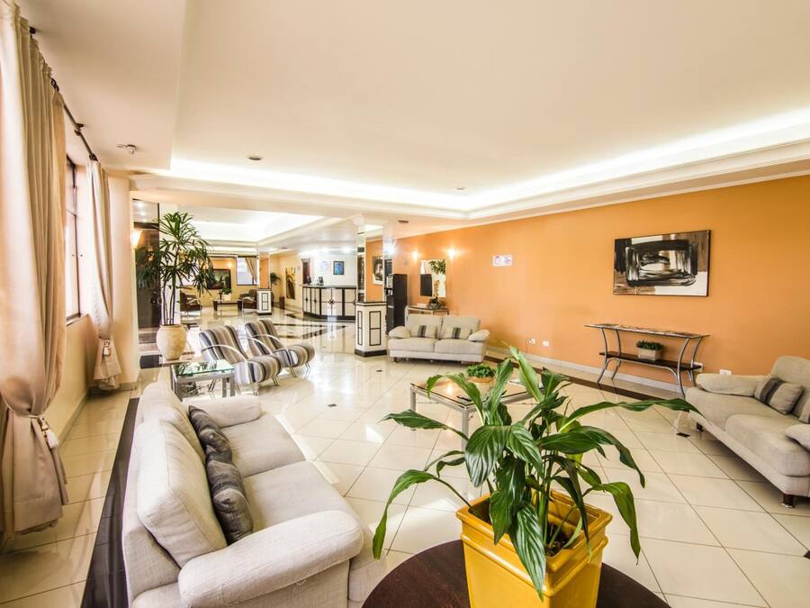A spacious living area with a sofa, armchairs, a coffee table, and a yellow plant.