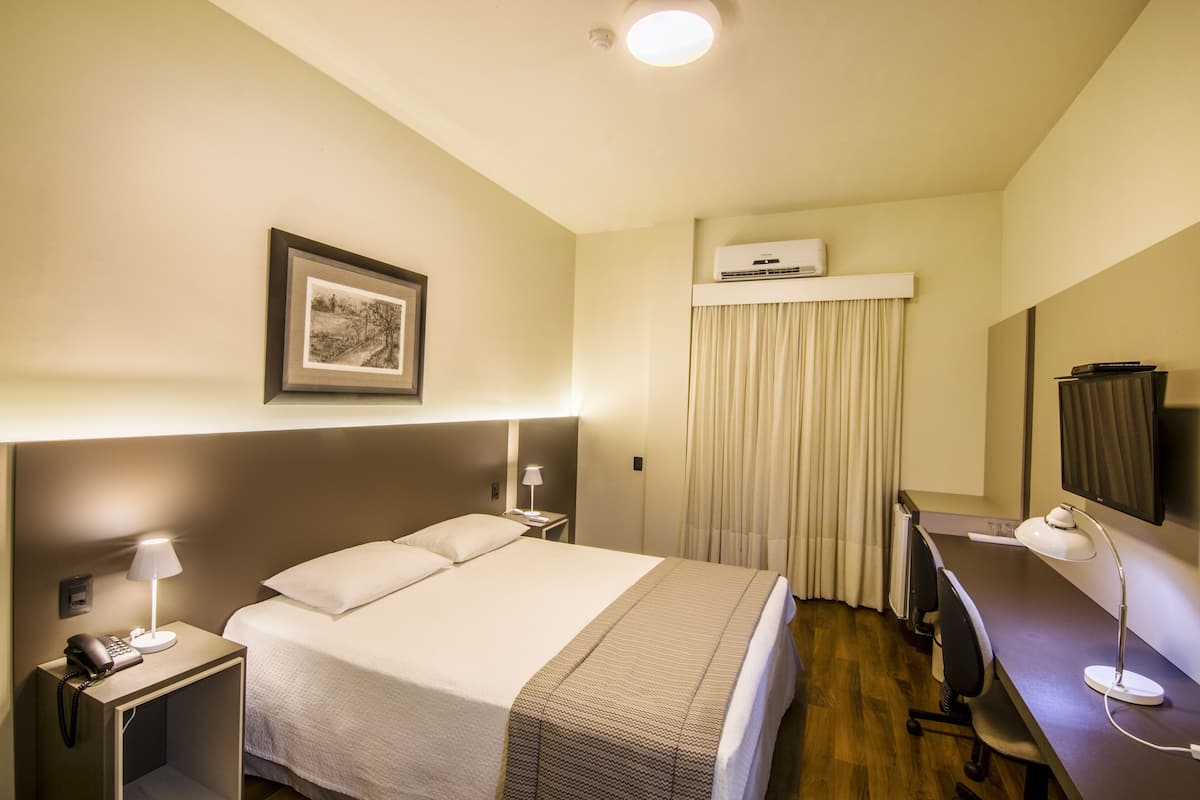 Habitación de hotel con cama, lámparas de noche, escritorio con silla, televisor de pantalla plana y aire acondicionado.