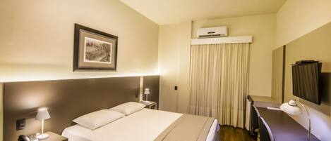 Habitación de hotel con cama, lámparas de noche, escritorio con silla, televisor de pantalla plana y aire acondicionado.