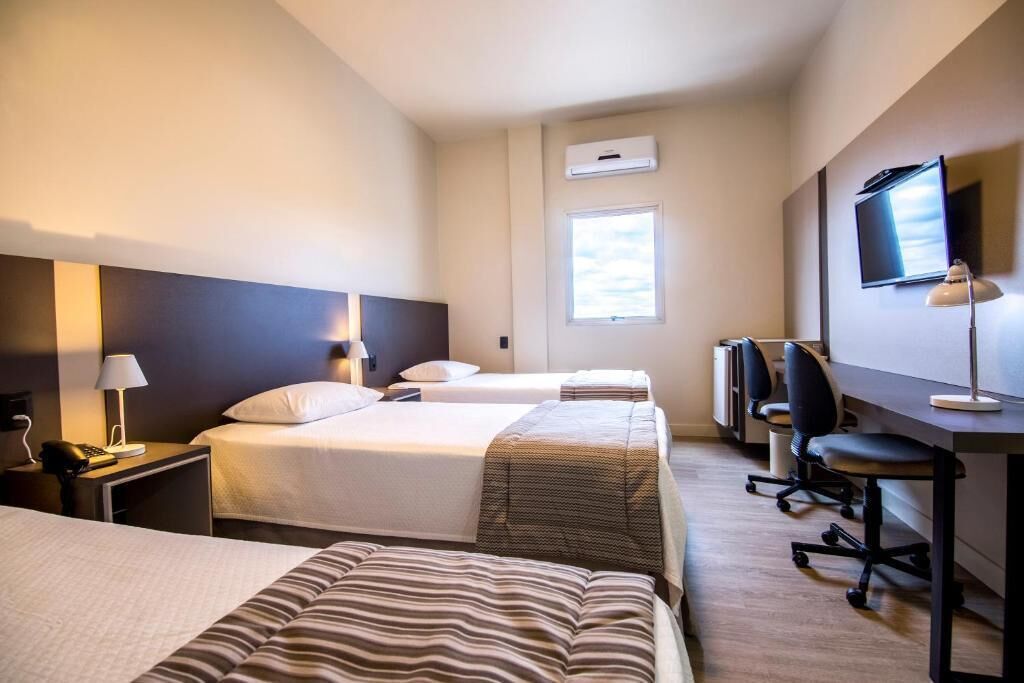 A hotel room with two beds, a desk, a chair, a TV, and a window.