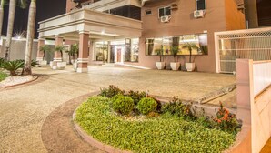 A multi-story hotel with a central courtyard, palm trees, and a well-lit entrance. - JR Hotel (Marilia)