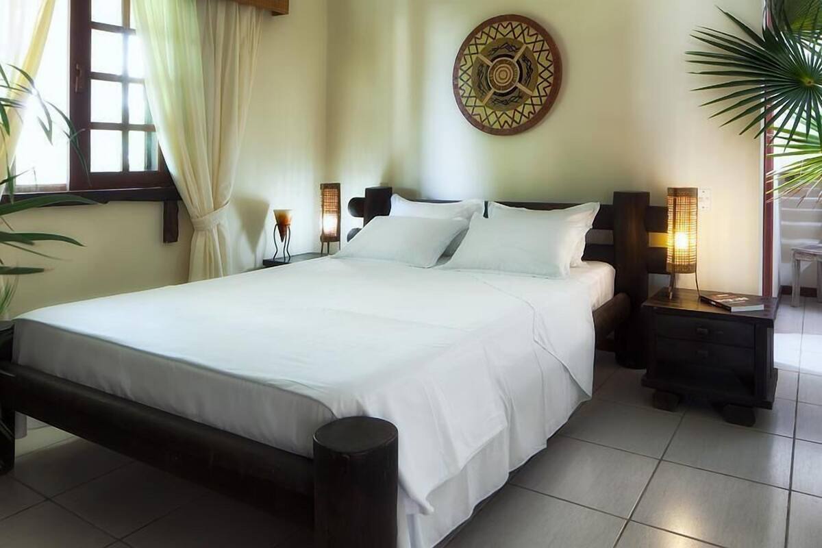 Una cama bien hecha con sábanas blancas, un cabecero de madera y dos mesitas de noche con lámparas.