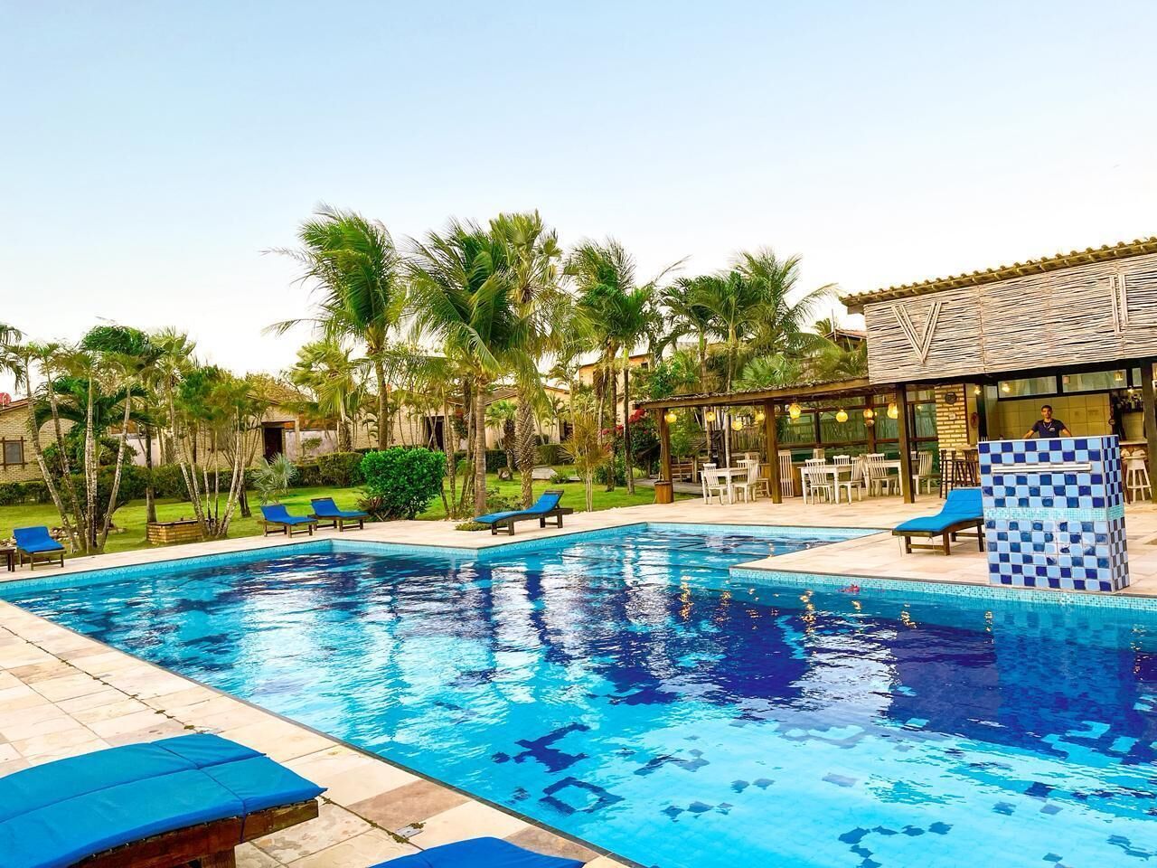 A swimming pool with lounge chairs, palm trees, and a building with a tiled roof.