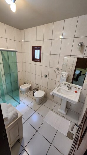 A bathroom with white tiles, a glass shower enclosure, two toilets, a sink, and a small window. - Eco Resort Vento Leste (Jijoca de Jericoacoara)