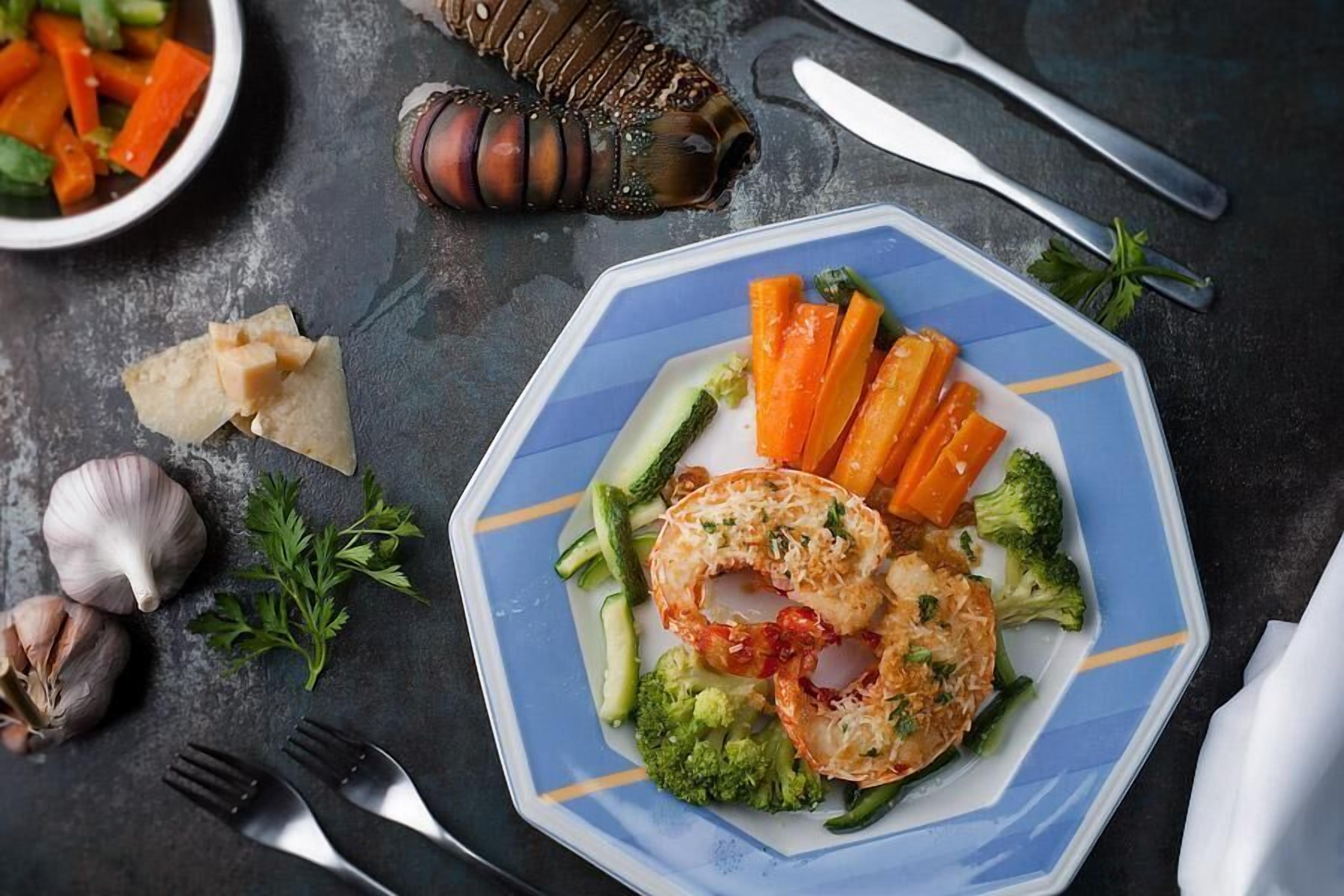 A plate of food with vegetables and a lobster tail on a dark surface.