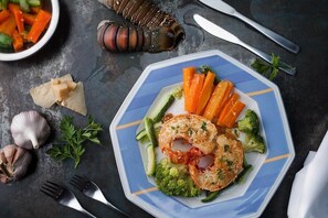 A plate of food with vegetables and a lobster tail on a dark surface. - Eco Resort Vento Leste (Jijoca de Jericoacoara)