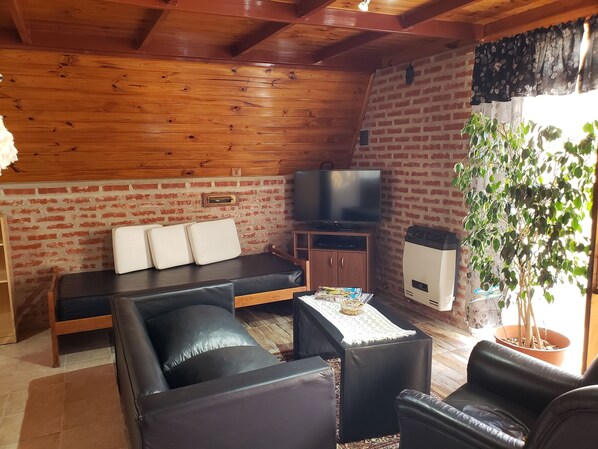A cozy living room with a sofa, a black leather couch, a television, and a potted plant.