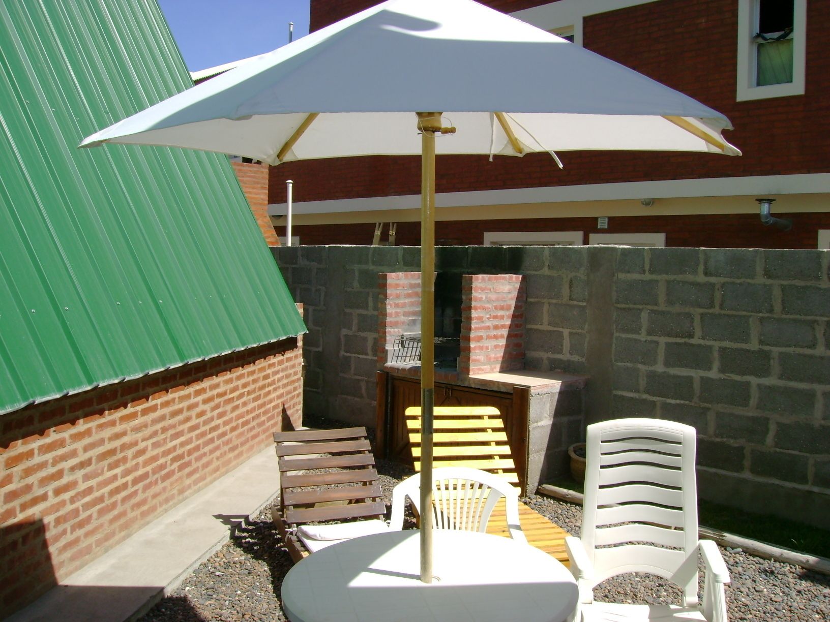 Un patio con una mesa redonda, dos sillas blancas y un gran paraguas.