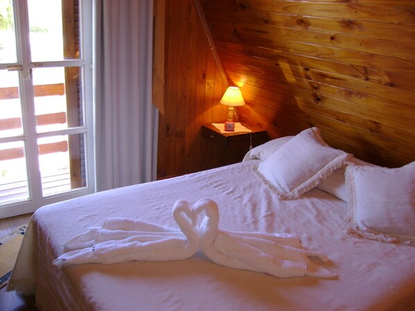 A neatly made bed with white linens and a towel arranged in a heart shape.