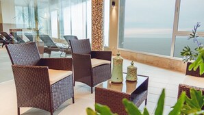 A modern lounge area with wicker furniture, a decorative column, and a view of the sea. - Hotel Las Rocas (Mar del Plata)