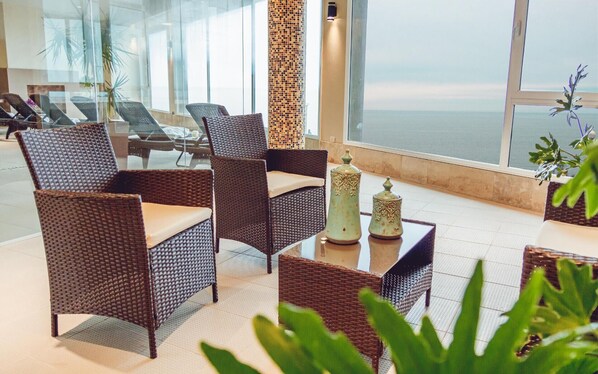 A modern lounge area with wicker furniture, a decorative column, and a view of the sea. - Hotel LAS Rocas (Mar del Plata)
