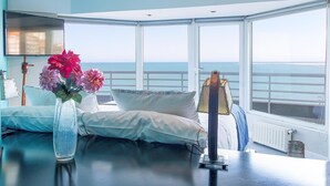 A room with a large window overlooking the sea, a bed with white linens, a vase with flowers, and a lamp on a table. - Hotel Las Rocas (Mar del Plata)