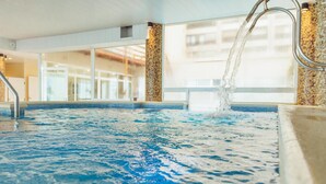 An indoor swimming pool with clear water, a metal faucet, and a view of a building through large windows. - Hotel Las Rocas (Mar del Plata)