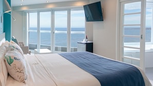 A bedroom with a large bed, a TV mounted on the wall, and a view of the sea through large windows. - Hotel Las Rocas (Mar del Plata)