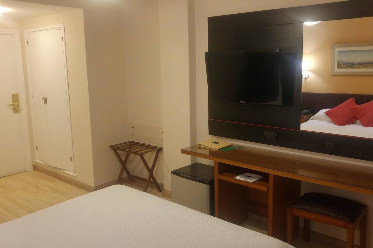 A hotel room with a bed, a TV, a desk with a chair, and a small table.
