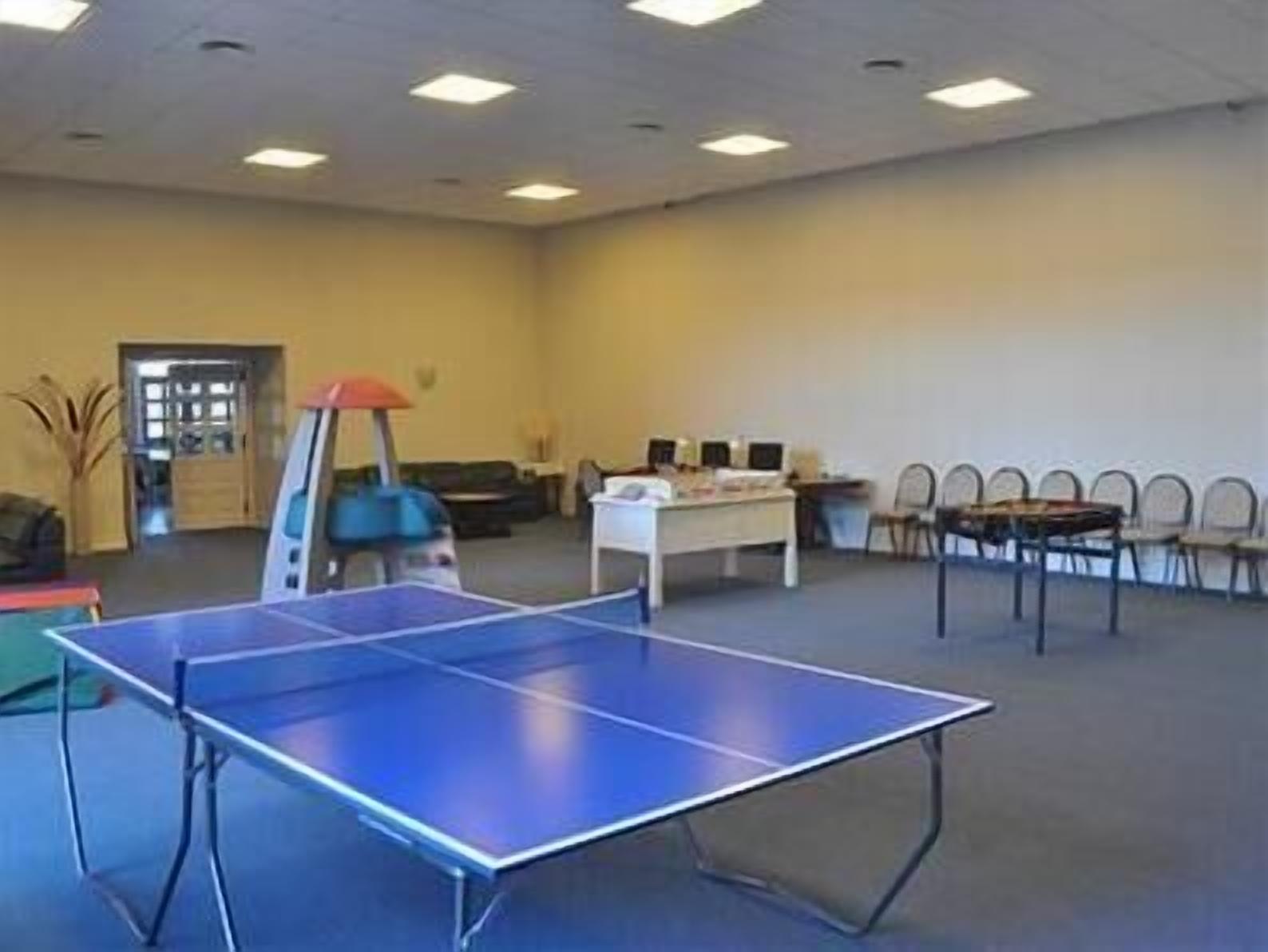 Una habitación con mesa de ping pong, escritorio con computadoras y varias sillas.