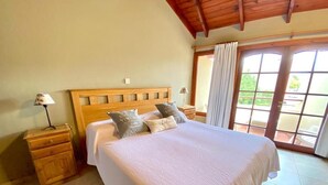 Un dormitorio con una cama de madera, una mesita de noche, una lámpara y vistas al exterior a través de una ventana.