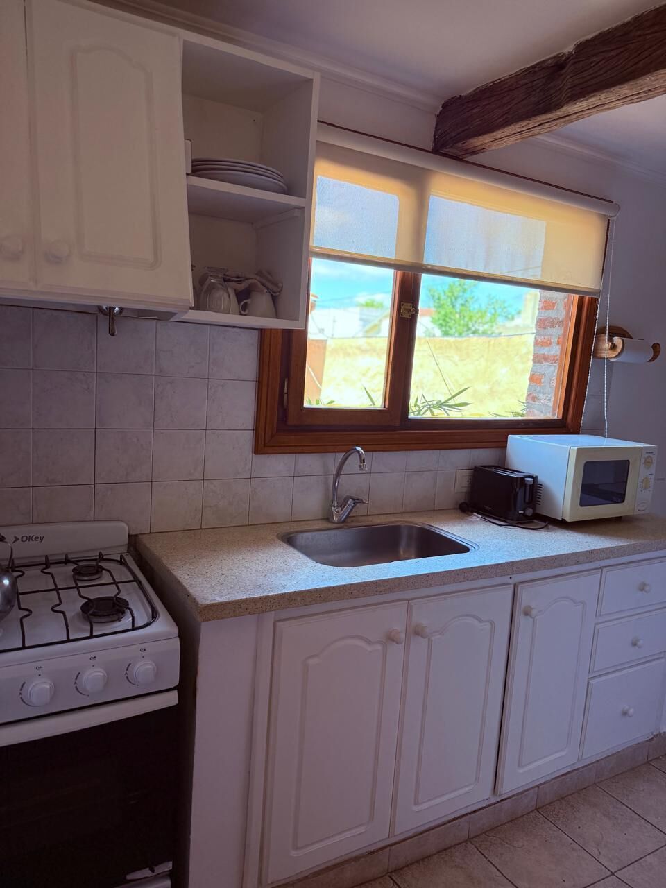 Una cocina con armarios blancos, estufa a gas, microondas y ventana con vista al exterior.