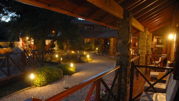 Un área de estar al aire libre con techo, muebles de madera y un sendero de grava.