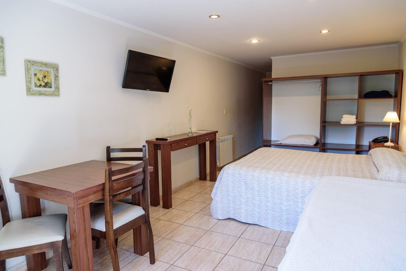 Una habitación de hotel con una cama, un escritorio con una silla, un televisor montado en la pared y un armario.