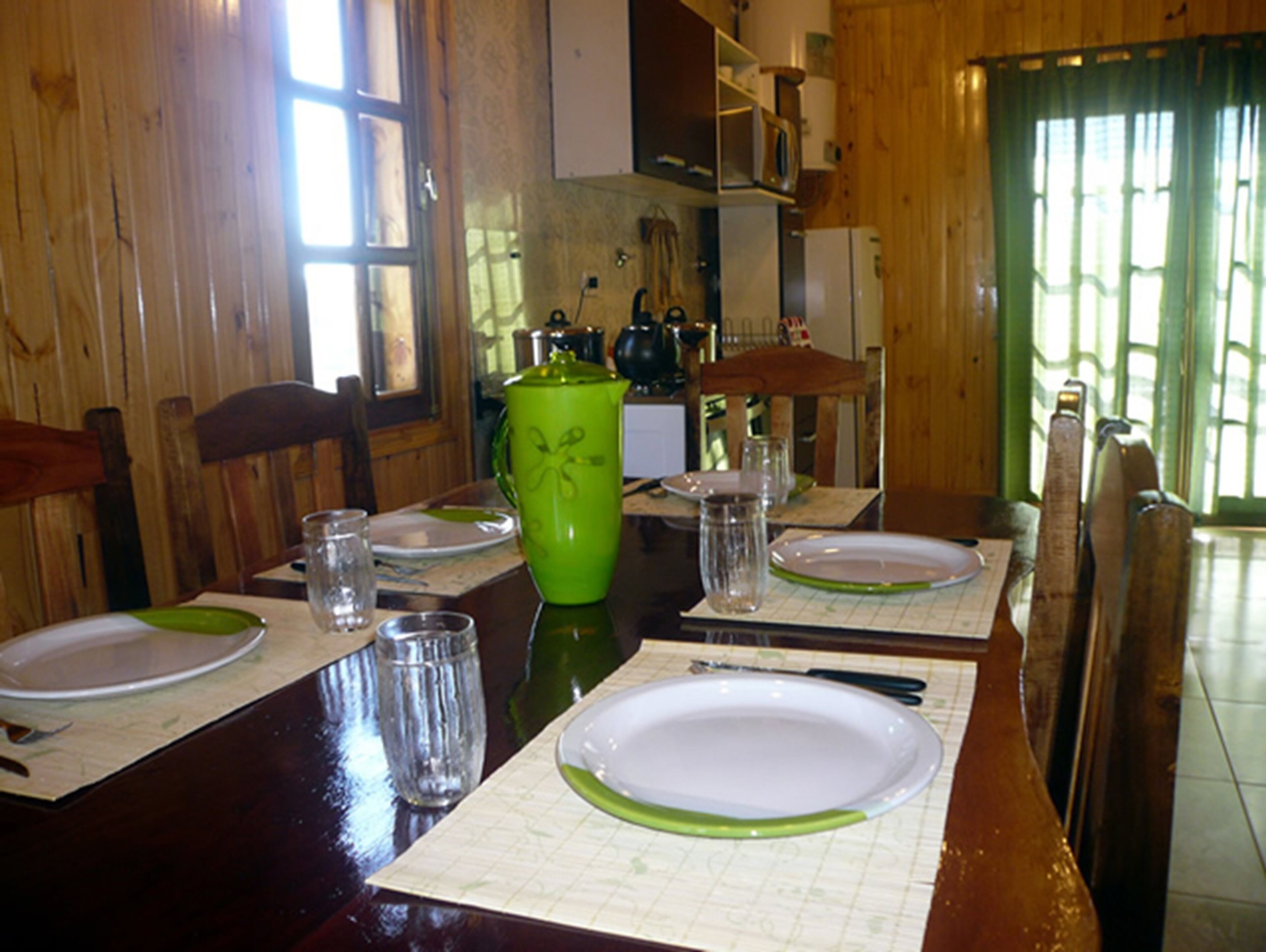 A wooden dining table with plates, glasses, and a green pitcher.
