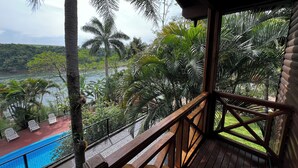 Una terraza de madera con piscina y sillas de descanso, con vistas a un río y abundante vegetación.