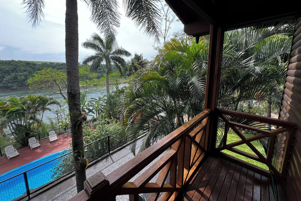 Une terrasse en bois avec une piscine et des chaises longues, offrant une vue sur une rivière et une végétation luxuriante.