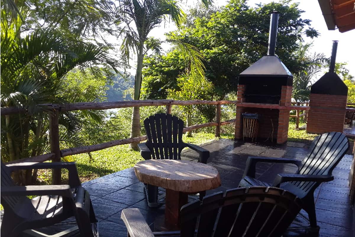 Une terrasse extérieure avec des chaises en bois et une petite table ronde, un barbecue en briques et une clôture en bois.