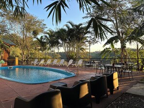 A pool area with lounge chairs and tables, surrounded by palm trees and a view of the landscape. - Costa del Sol Iguazú (Puerto Iguazú)