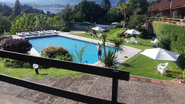 Piscina con sillones de playa y sombrillas, rodeada de vegetación y vistas a montañas.