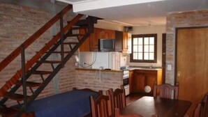 Una cocina con una escalera de madera, una mesa de comedor con sillas y una ventana.