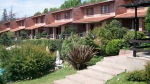 Una hilera de edificios de ladrillo con balcones, rodeada de abundante vegetación y un cielo despejado.