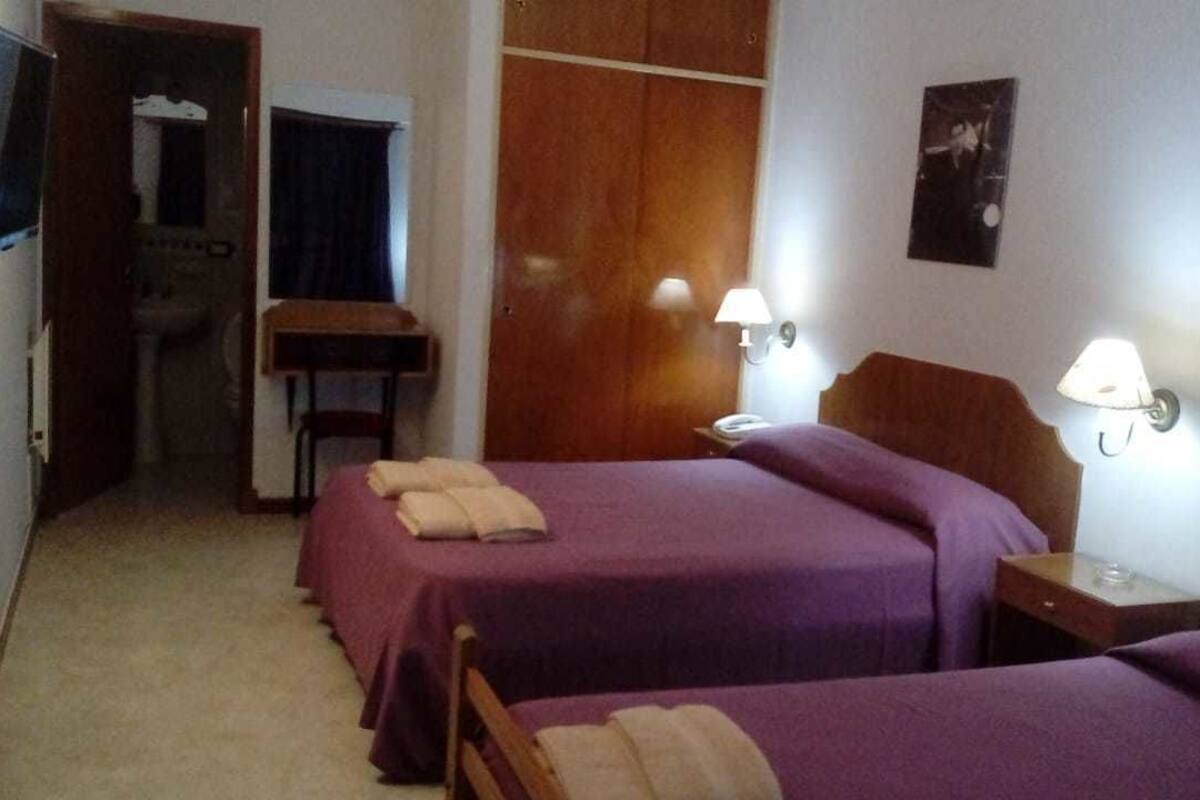 Habitación de hotel con dos camas, un armario de madera, una mesita pequeña y dos lámparas de noche.