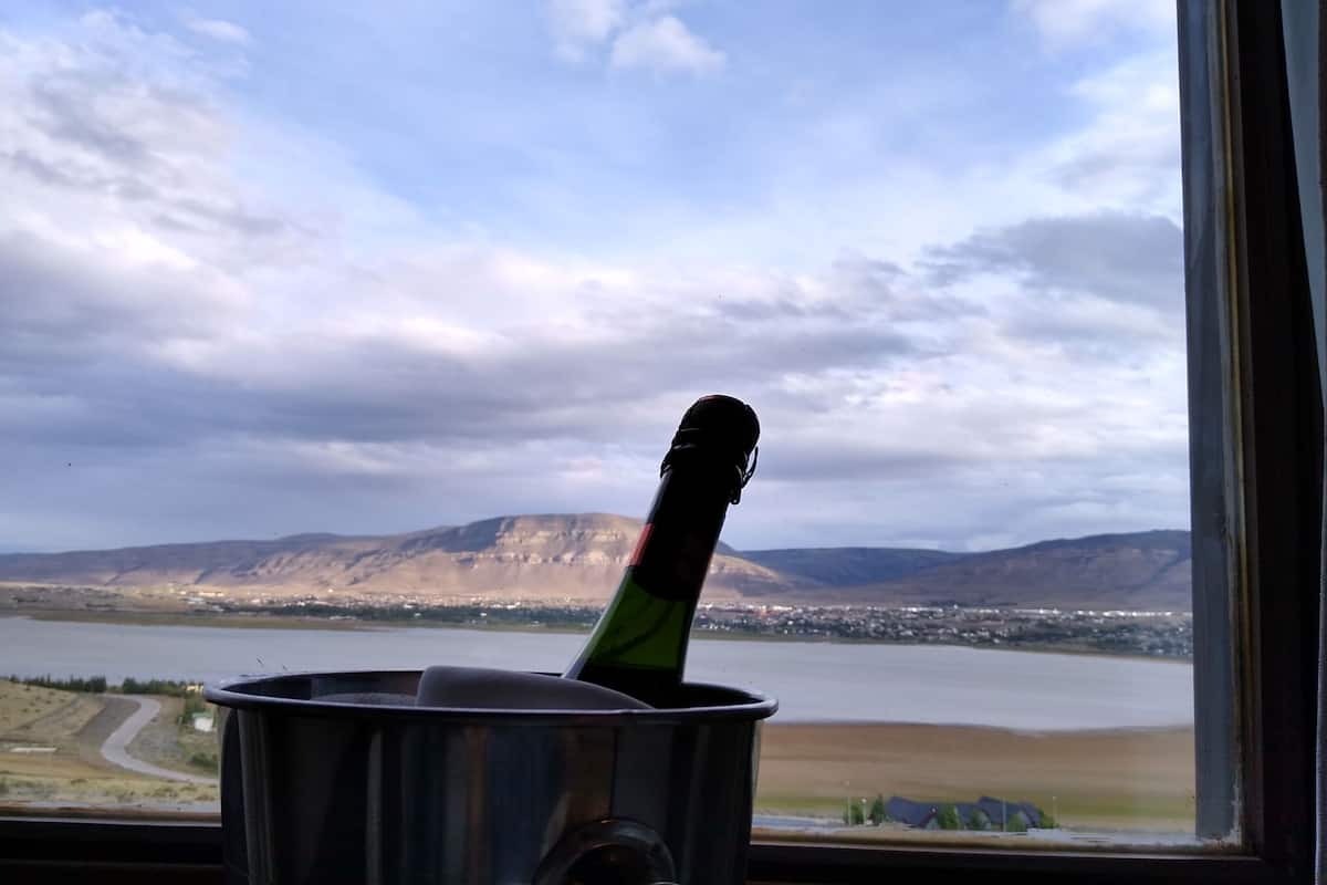 Garrafa em recipiente metálico, com vista para um lago e montanhas através de uma janela.