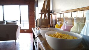Eine Küche mit Holzschränken, einem Holztisch und einem Fenster. Auf dem Tisch stehen Schalen mit Essen und Flaschen mit Saft.