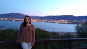 Uma pessoa está em uma varanda com vista para a água e luzes da cidade ao longe.