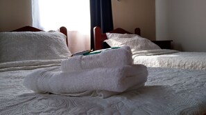 Cama bem arrumada com lençóis brancos e uma toalha dobrada em cima.