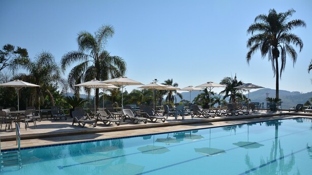 Une piscine entourée de chaises longues et de parasols, avec des palmiers et des montagnes en toile de fond.
